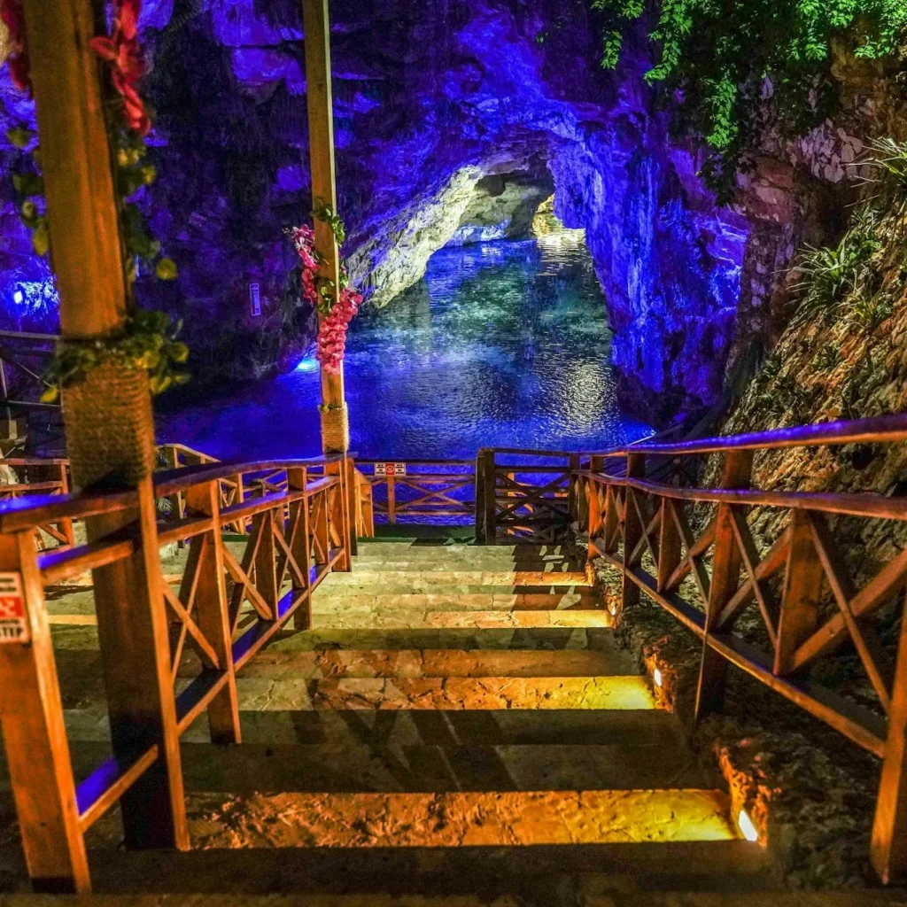 Stairs leading to a vibrant cave pool in Punta Cana, illuminated by colorful lights, perfect for adventure seekers.