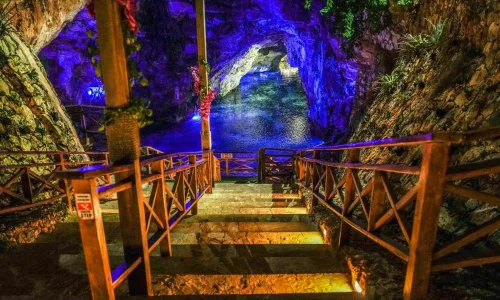 Stairs leading to a vibrant cave pool in Punta Cana, illuminated by colorful lights, perfect for adventure seekers.