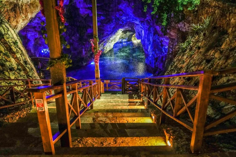 Stairs leading to a vibrant cave pool in Punta Cana, illuminated by colorful lights, perfect for adventure seekers.